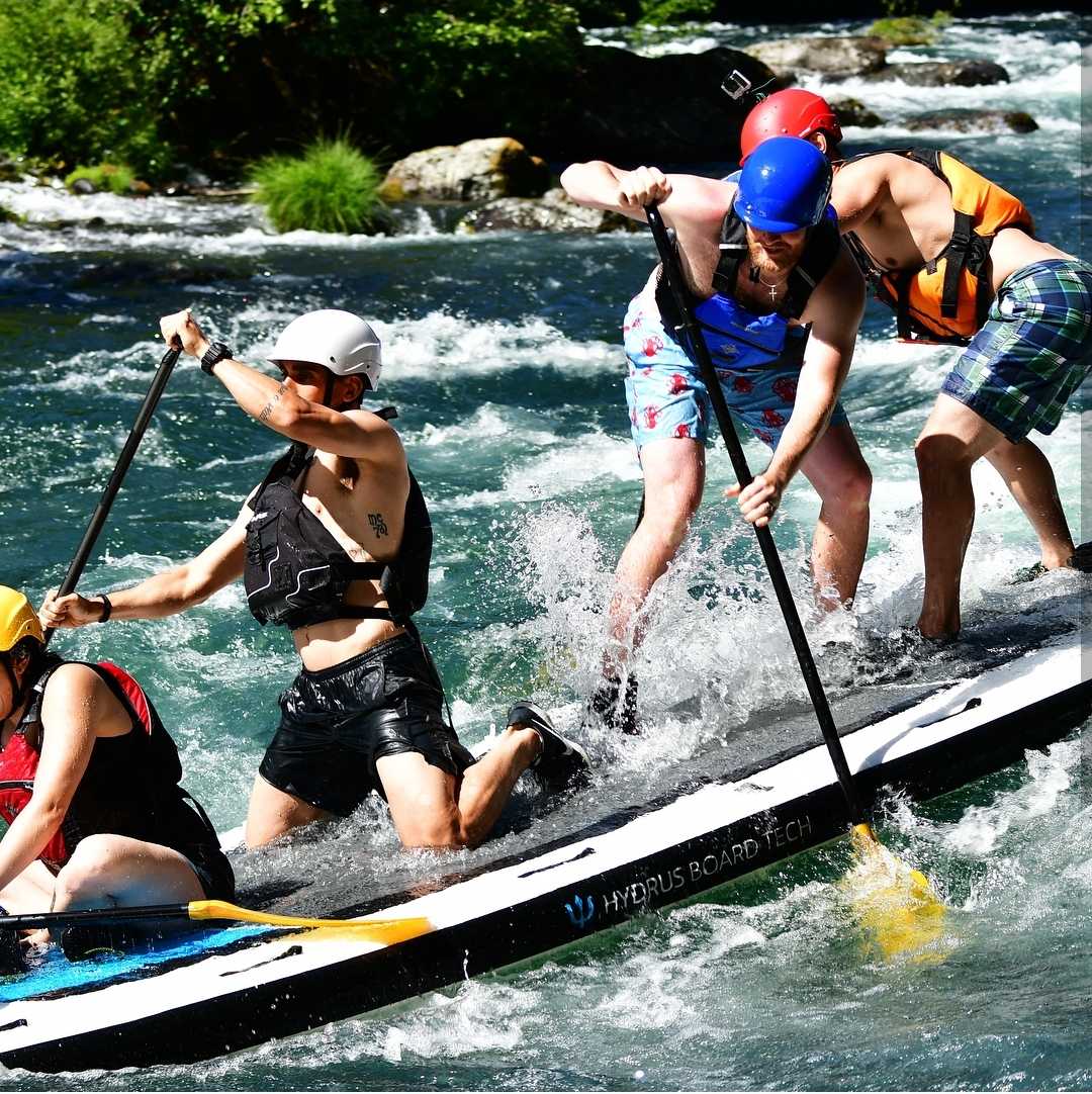 Individuals ride a paddleboard over whitewater.