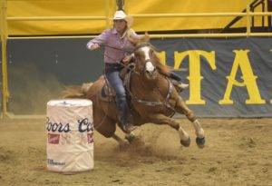 An individual rides a horse around a barrel.