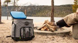 A Cordova cooler sits on the sand next to a lake.