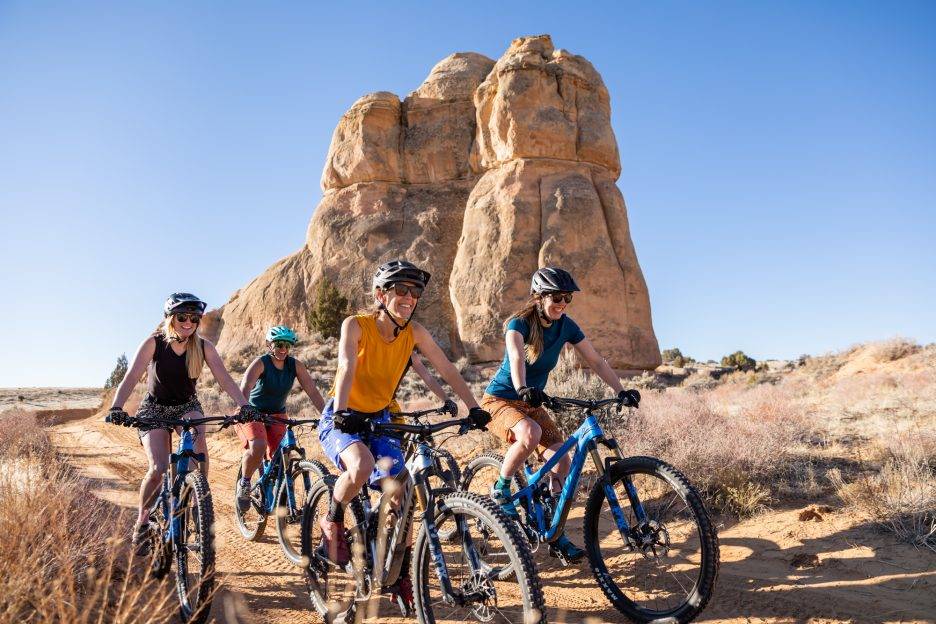 A group of women sporting Wild Rye gear ride bikes through the desert. 