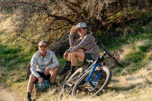 Two people resting on a hillside next to a mountain bike