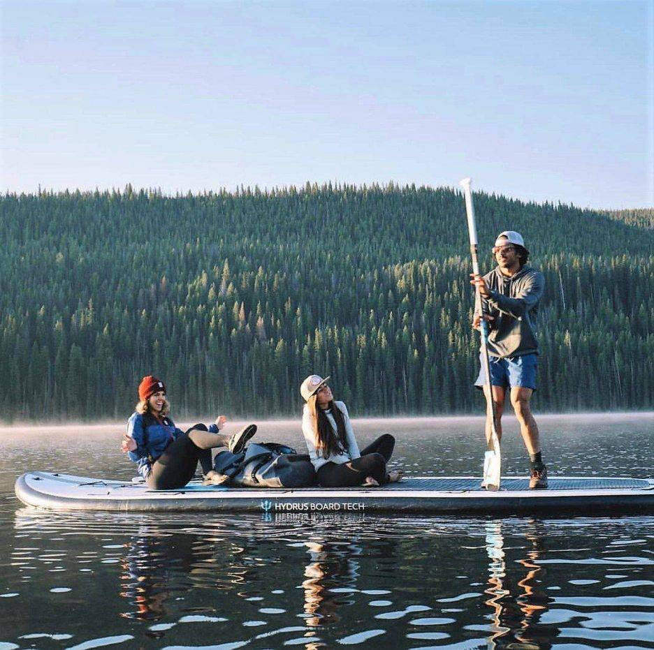 Three peole on an inflatable paddleboard on a lake